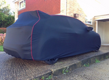A navy blue fleece car cover with red trim fitted on a car outdoors.