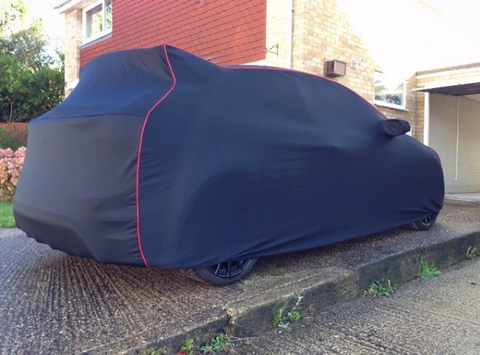 A navy blue fleece car cover with red trim fitted on a car outdoors.