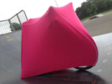 A bright pink fleece cover for a road bike mounted on a smart trainer, with a white piping detail.